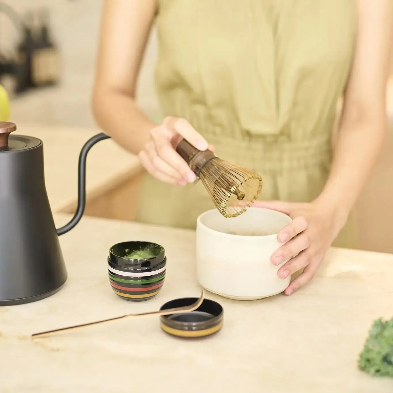 Przygotowanie herbaty matcha przy użyciu bambusowej miotełki chasen w ceramicznej misce, z czajnikiem i akcesoriami na blacie