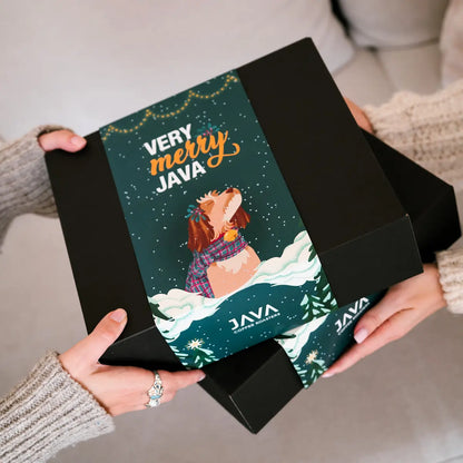 Świąteczne pudełko prezentowe JAVA Coffee z grafiką Very Merry Java i ilustracją psa, trzymane w dłoniach.