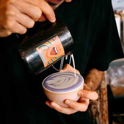 Barista przygotowujący fioletowe latte z ube z delikatnym latte art w ceramicznej filiżance