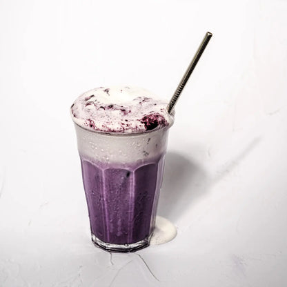 Fioletowe iced latte z ube i mleczną pianką podane w szklance ze słomką na jasnym tle