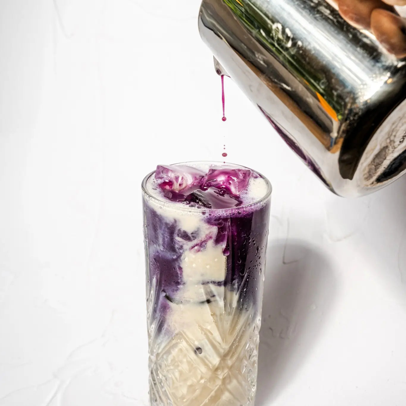 Przygotowanie mrożonego fioletowego latte z ube i mlekiem nalewanego do szklanki z lodem na jasnym tle