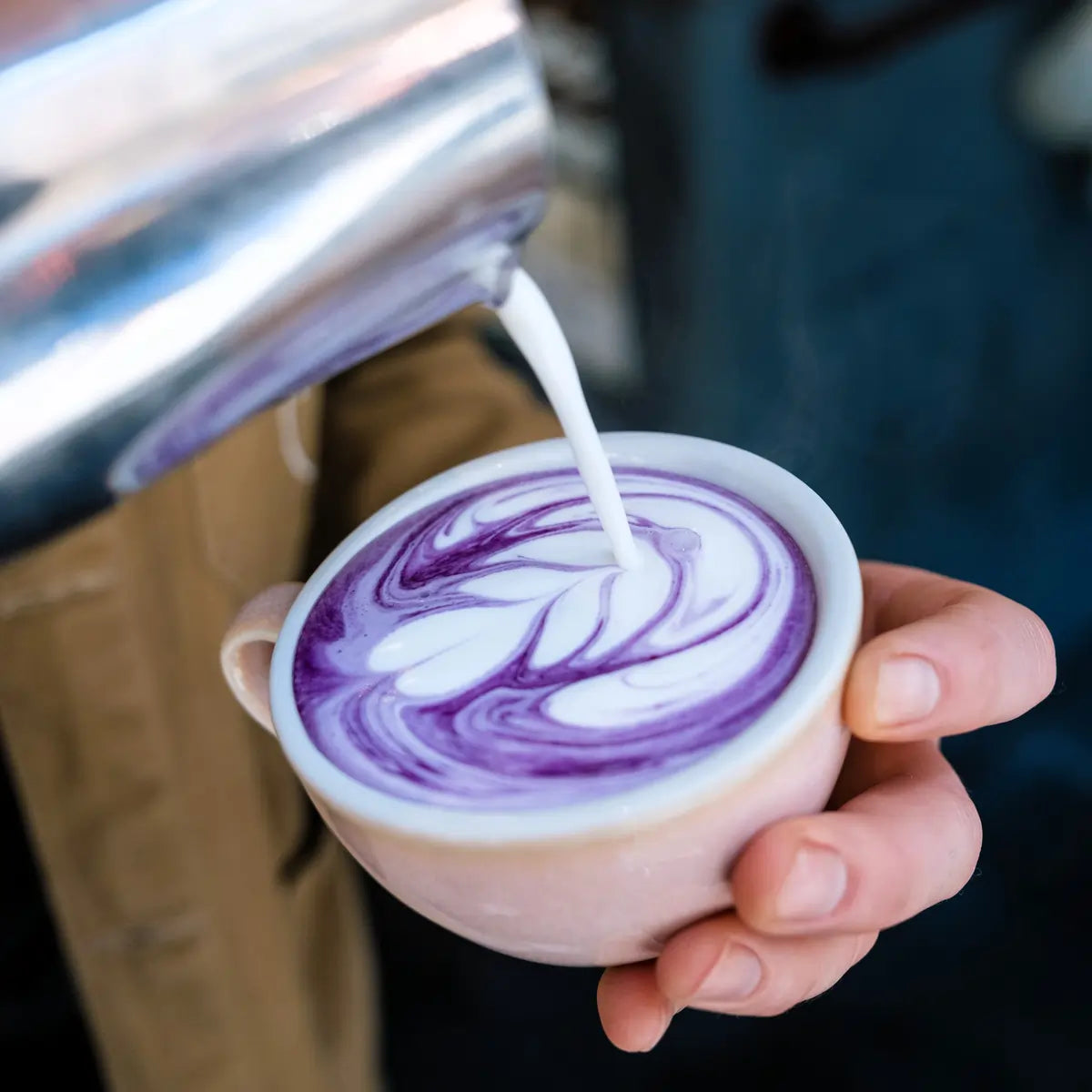 Fioletowe latte z ube z artystycznym latte art przygotowywane przez baristę w filiżance ceramicznej
