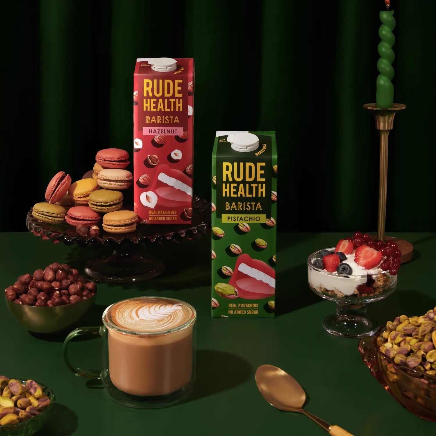 Napój roślinny Rude Health Barista Pistachio 1L na złotej tacy z filiżanką kawy i miską pistacji, na tle ciemnozielonej zasłony, bez dodatku cukru i oleju.
