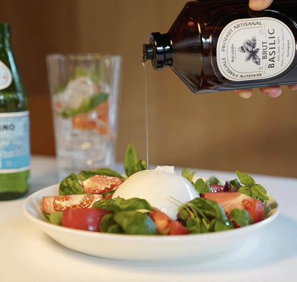 Sałatka z mozzarellą, pomidorami i świeżą bazylią na białym talerzu, z polewaniem oliwy z butelki z bazylią, idealna na lekkie danie, naturalne składniki.