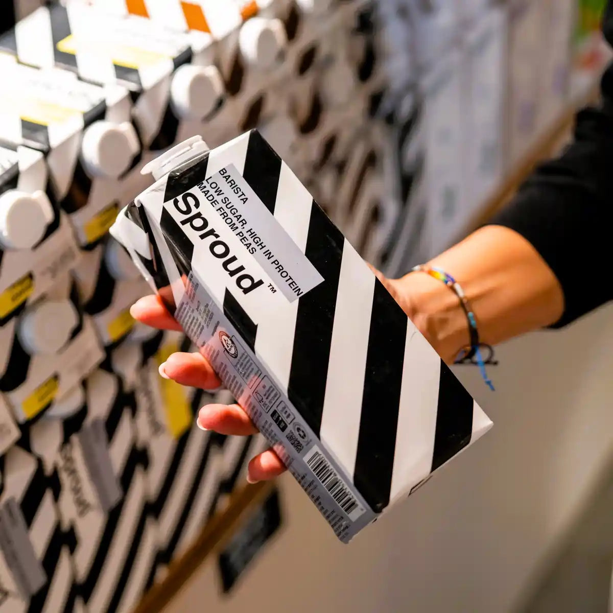 Karton napoju roślinnego Sproud Barista 1L trzymany w dłoni na tle półki sklepowej – wegański napój z grochu do kawy, bogaty w białko i o niskiej zawartości cukru.