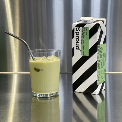Karton napoju roślinnego Sproud Matcha 1L obok szklanki z lodami i metalową słomką, ujęcie na tle kuchennym