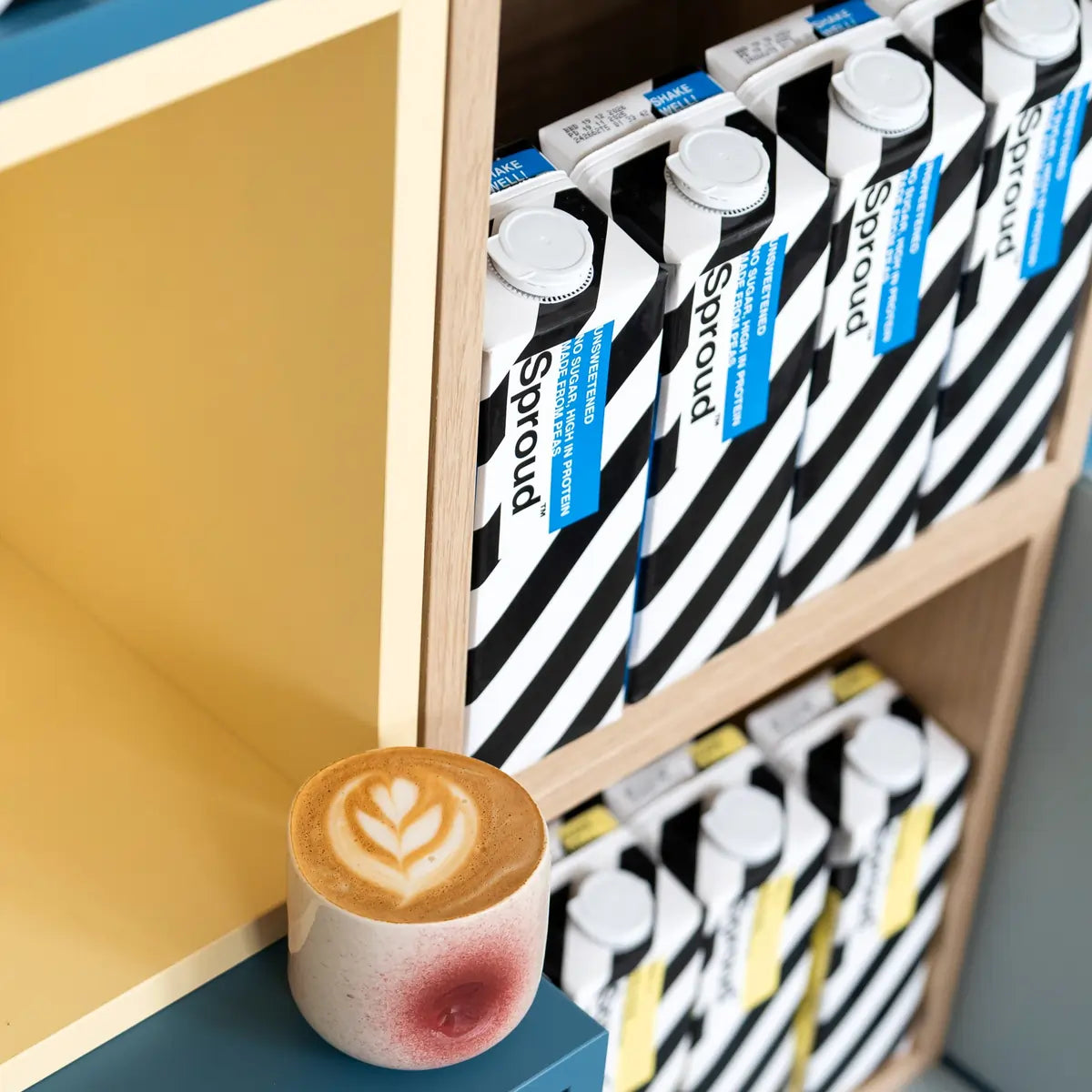 Kawa z latte art oraz napoje roślinne Sproud Unsweetened i Vanilla na półce w Java Coffee Roasters w Warszawie – roślinna alternatywa mleka do kawy specialty.