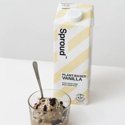 Sproud Mleko roslinne Vanilla w kartonie 1L na białym tle, obok deser w szklance udekorowany kawałkami czekolady i wiórkami kokosowymi.