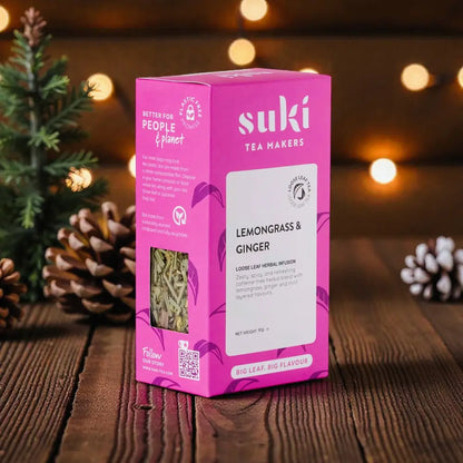 Herbata ziołowa Suki Lemongrass & Ginger 80 g na świątecznym tle z lampkami i szyszkami
