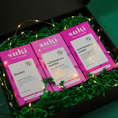 Zestaw trzech herbat Suki Tea w świątecznej aranżacji z zielonym wypełnieniem i lampkami – Bramble, Partridge in a Pear Tea oraz Lemongrass & Ginger