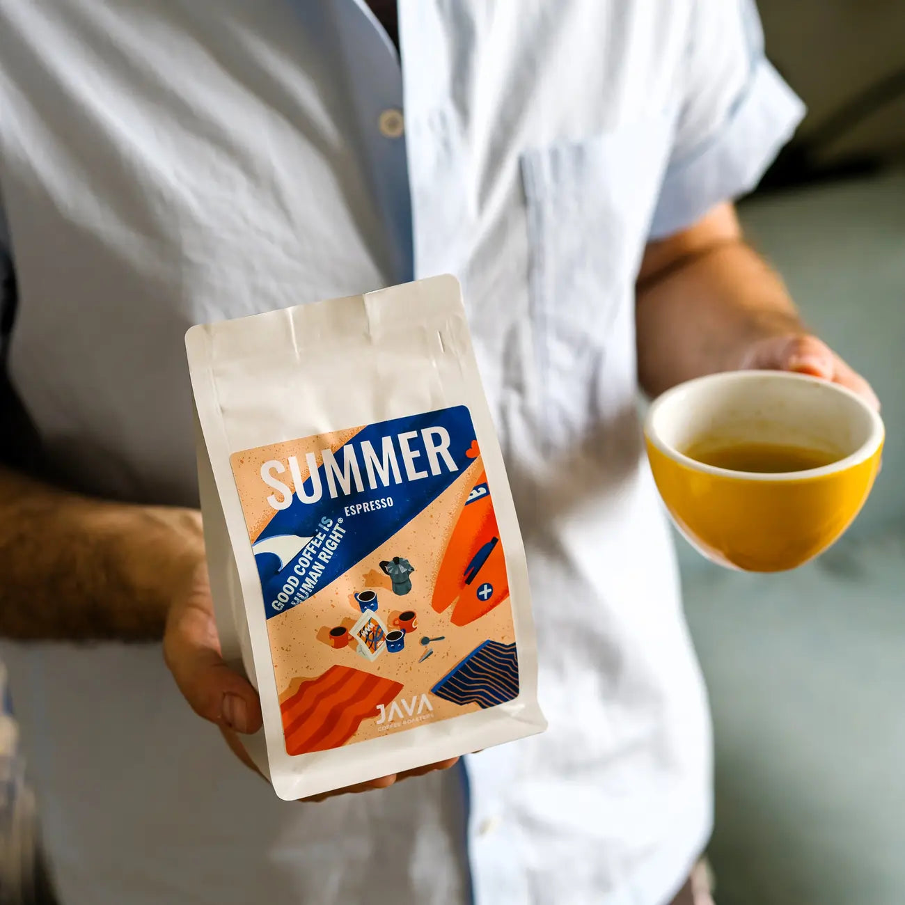 Paczka Summer Espresso od JAVA Coffee Roasters trzymana w dłoni obok filiżanki espresso w domowym wnętrzu