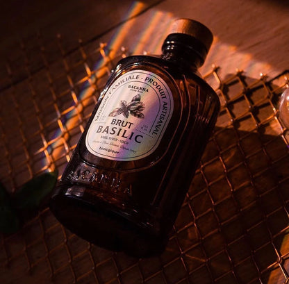 Butelka syropu bazyliowego BACANHA na metalowej siatce, podświetlona ciepłym światłem, idealna do napojów i deserów, naturalny i organiczny produkt.