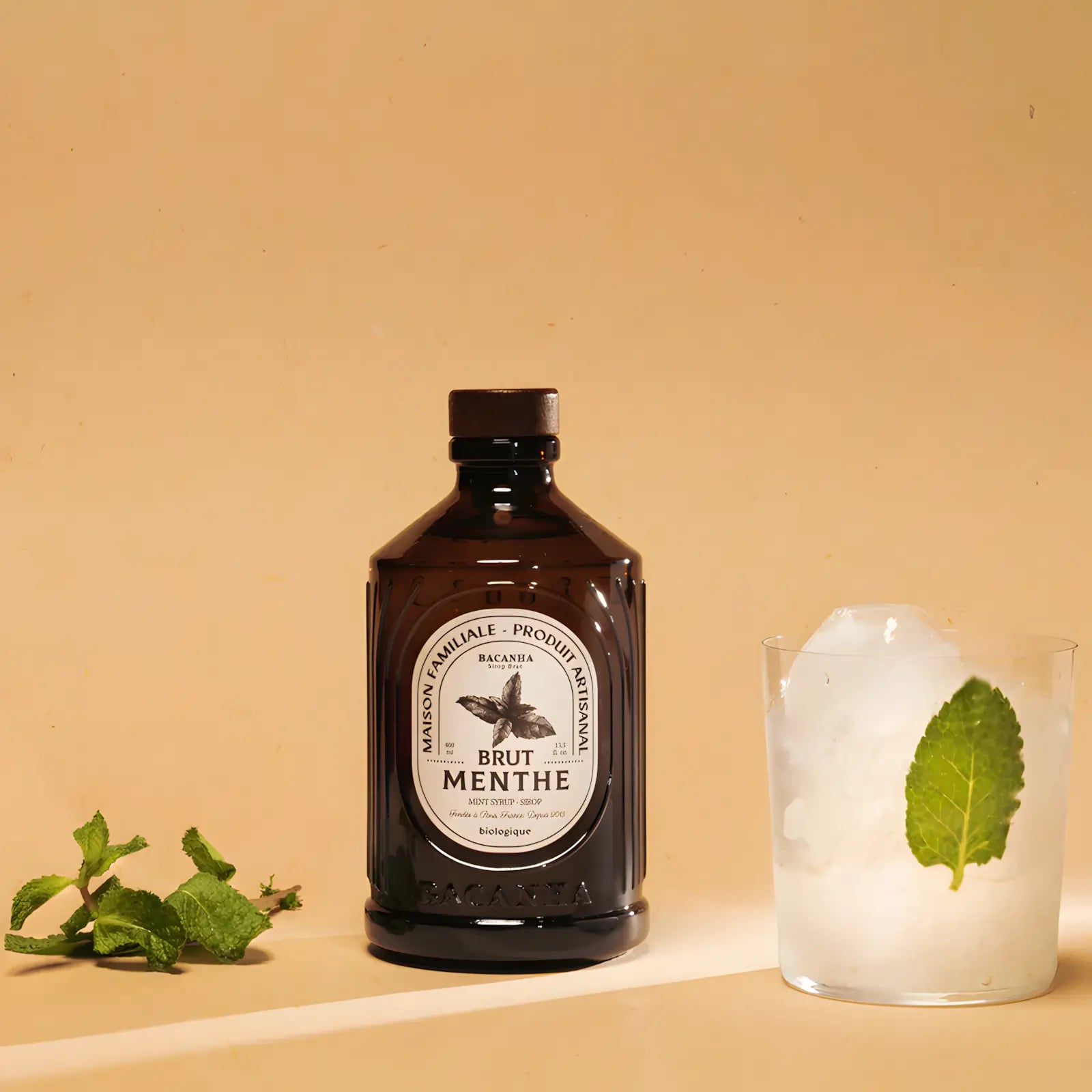 Syrop miętowy Bacanha Brut Menthe BIO – butelka syropu z miętą i szklanką napoju z lodem, zdjęcie lifestyle na jasnym tle