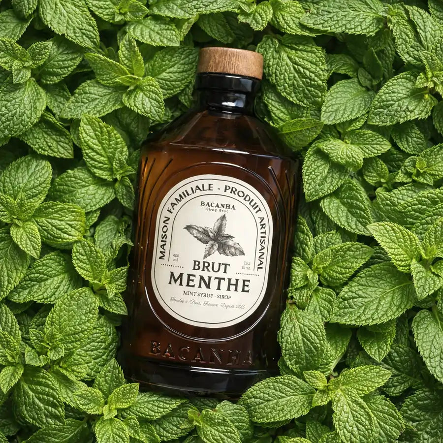 Syrop miętowy Bacanha Brut Menthe BIO – butelka syropu na tle świeżych liści mięty, zdjęcie inspirowane składnikiem