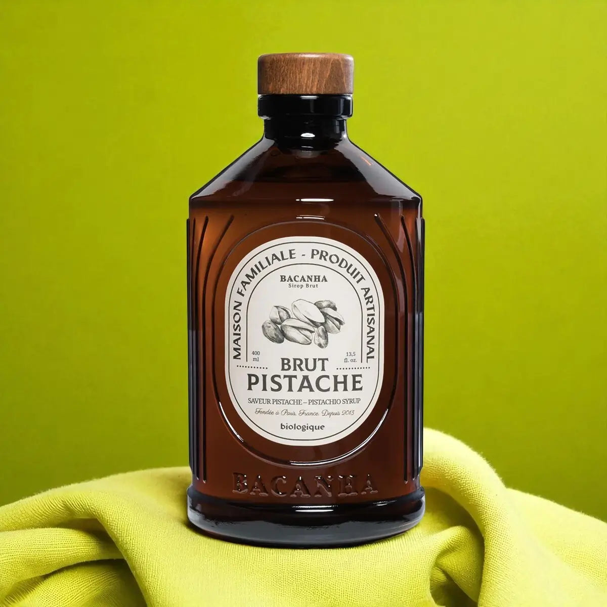 Butelka syropu pistacjowego Bacanha Brut Pistache 400 ml na drewnianym tle – naturalny syrop do kawy i koktajli