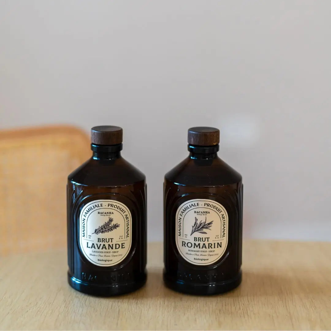 Zestaw dwóch syropów Bacanha – Lavande i Romarin – w brązowych butelkach, ustawionych na drewnianym stole