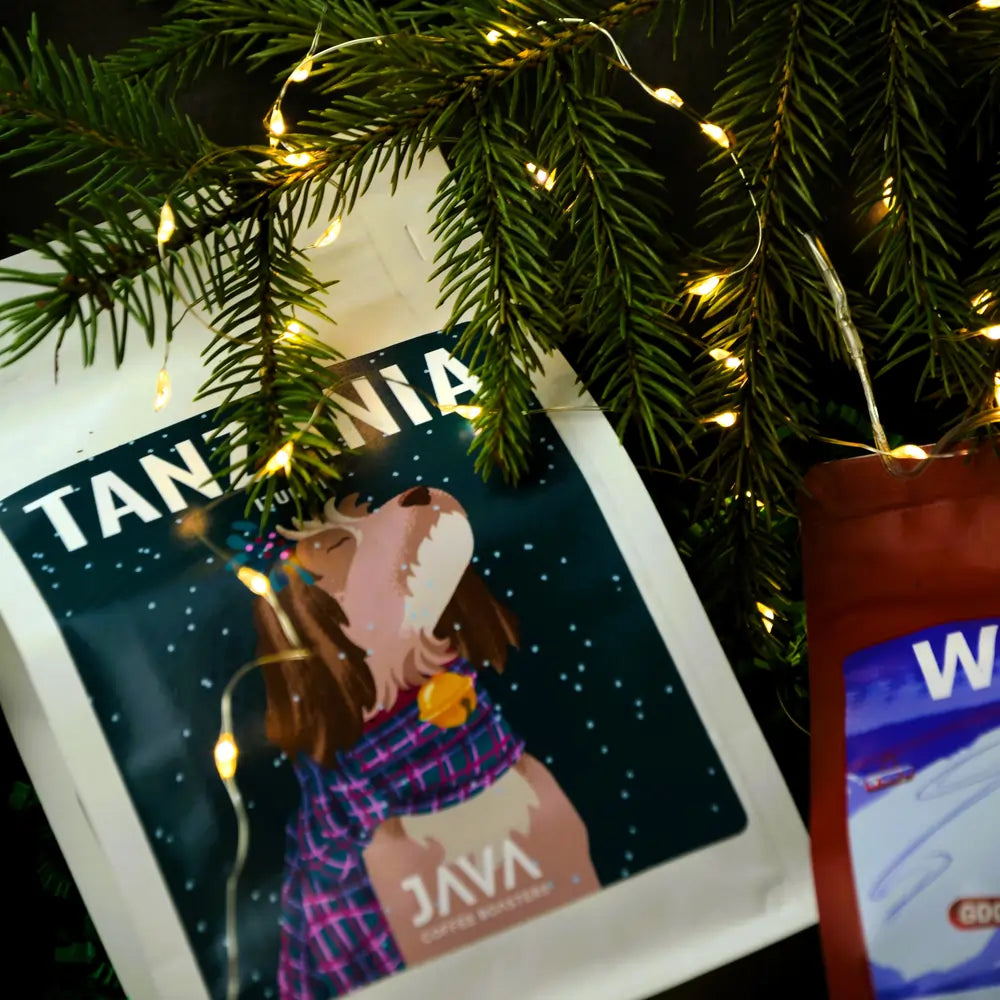 Kawa Tanzania JAVA Coffee w świątecznej aranżacji z gałązkami świerku i ciepłymi lampkami obok opakowania Winter Espresso.