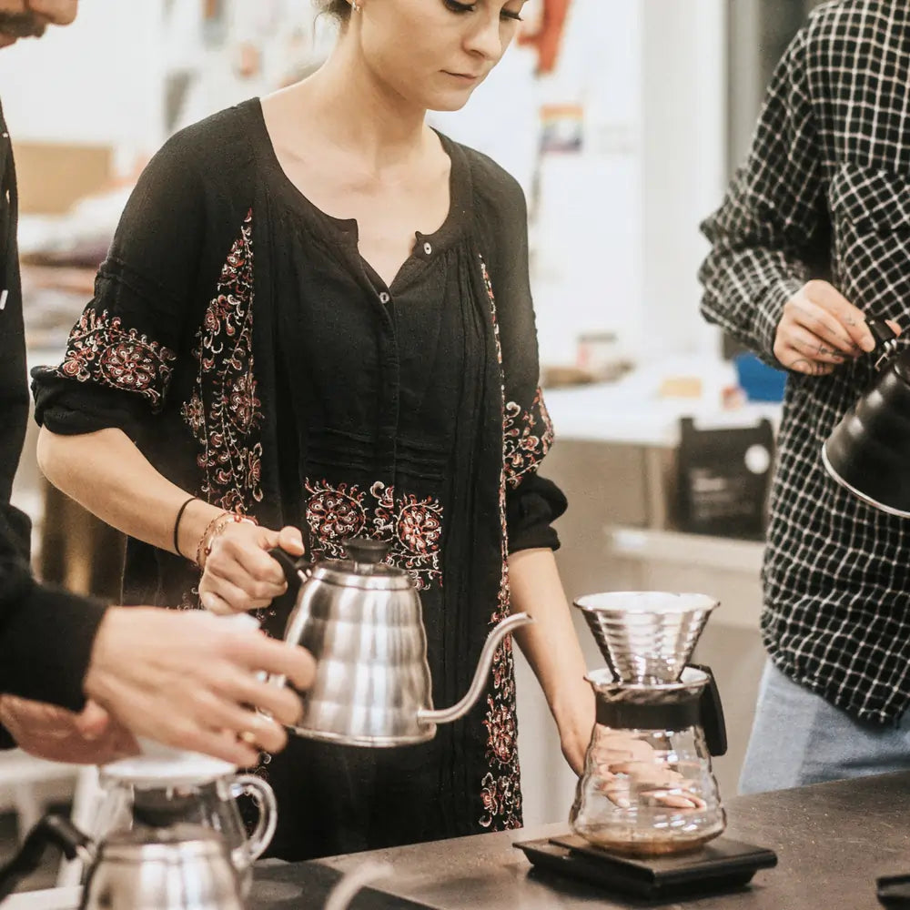 Uczestnicy warsztatów parzenia kawy przygotowują V60 z użyciem stalowych konewek i dripera.