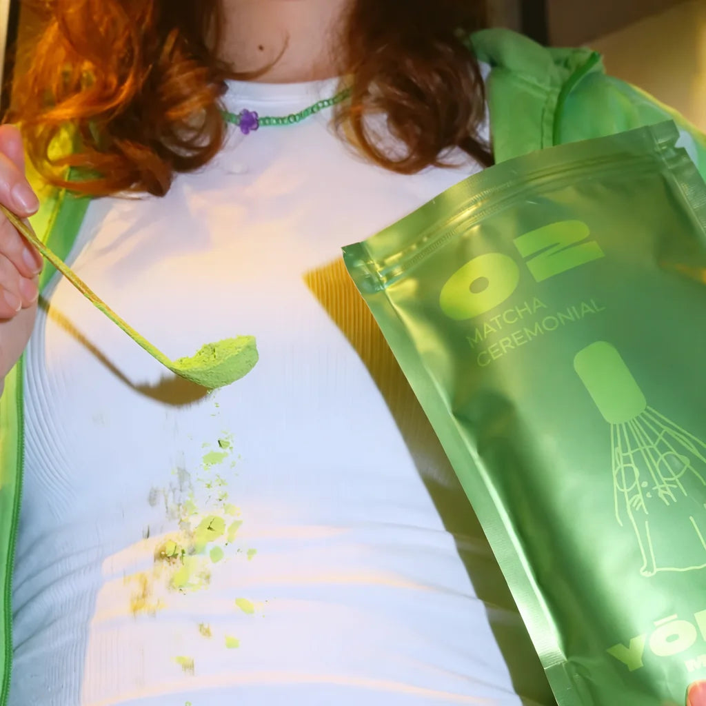 Lifestyle zdjęcie ceremonialnej matchy Yōkiro – zielony proszek matchy na łyżeczce bambusowej, opakowanie Yōkiro Matcha Ceremonial w tle