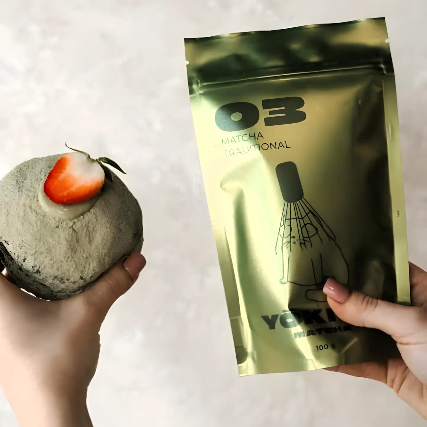 Lifestyle zdjęcie matchy Yōkiro Traditional – zielone opakowanie matchy trzymane w dłoni obok deseru z matchą i truskawką