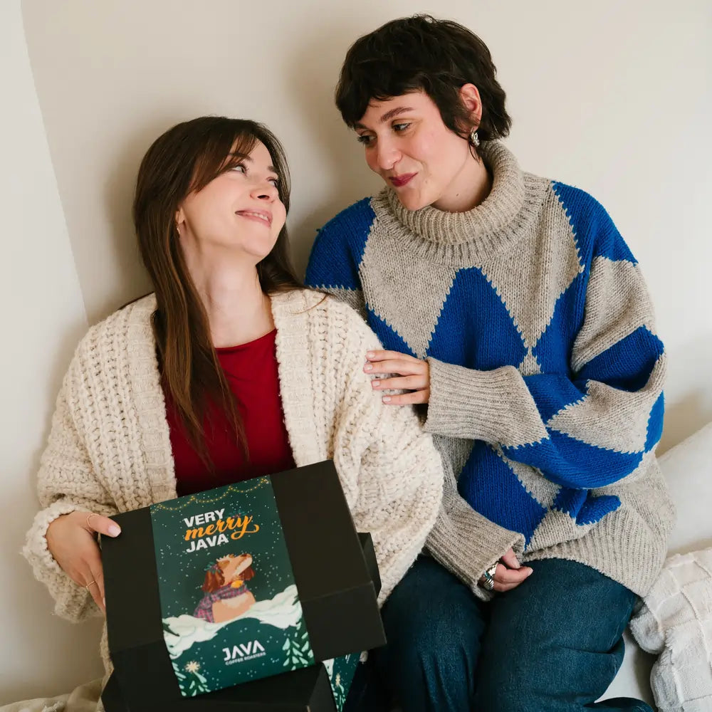 Dwie kobiety trzymające świąteczny zestaw prezentowy JAVA Coffee z czarnym pudełkiem i zimową grafiką Very Merry Java