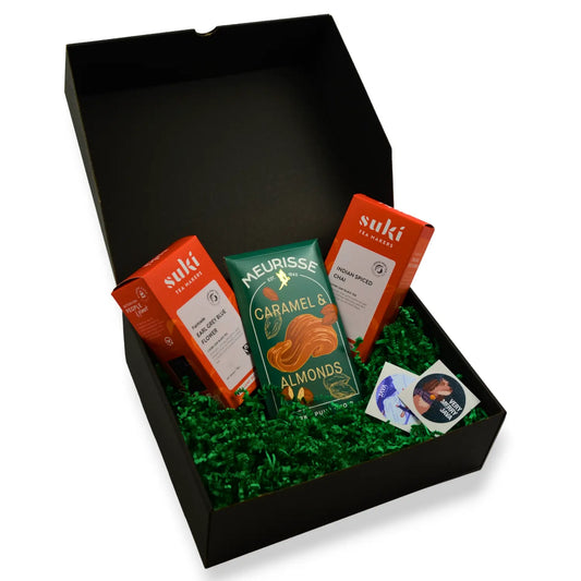 Świąteczny zestaw prezentowy z herbatami SUKI Tea Makers, czekoladą Meurisse Caramel & Almonds oraz dodatkami, zapakowany w czarne pudełko z zielonym wypełniaczem.